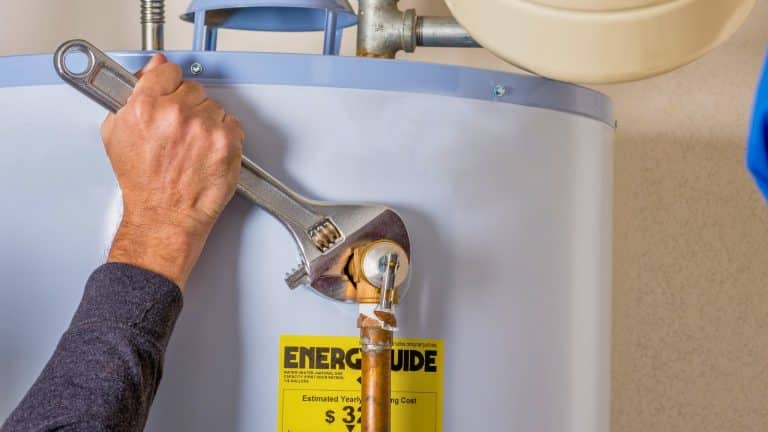 Plumber using a wrench to tighten a water heater connection during maintenance.
