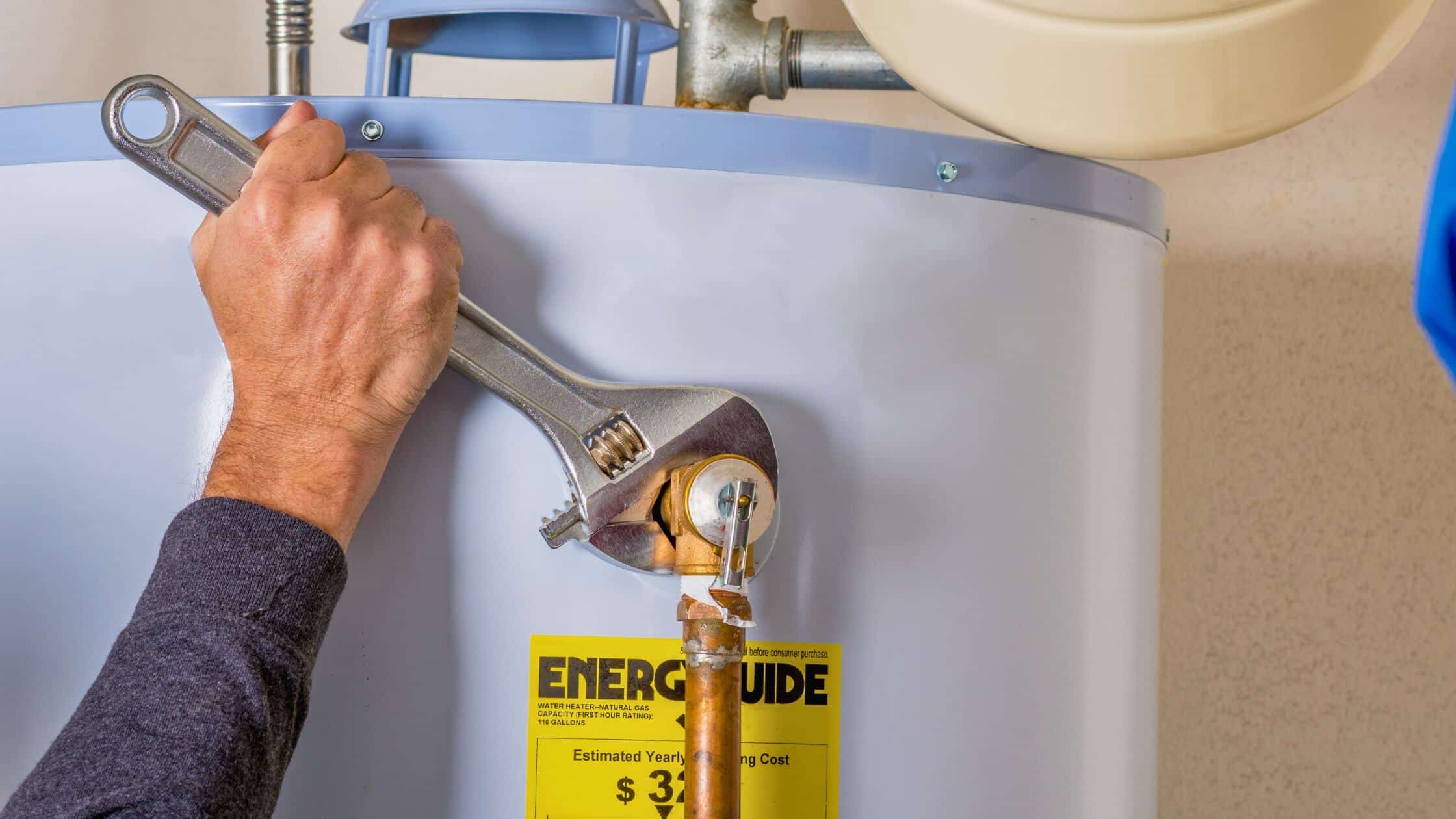 Plumber using a wrench to tighten a water heater connection during maintenance.